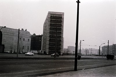 Mid-century Brutalist apartment block with exposed concrete façade and horizontal balconies, flanked by older low-rise buildi...