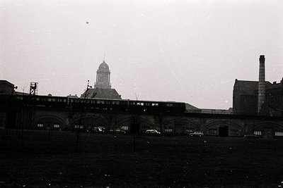 Black-and-white shot of a historic train station with arched brick viaducts, mid-20th century industrial architecture. Promin...