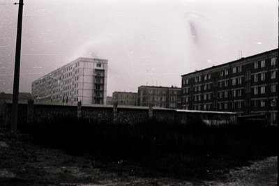 Mid-century Soviet-era apartment blocks with utilitarian concrete facades, likely from the 1960s-70s. Graffiti on lower walls...
