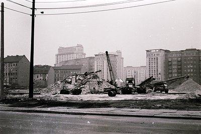 Black-and-white urban demolition scene featuring a mid-20th-century crane removing debris from collapsed brick structures. Su...