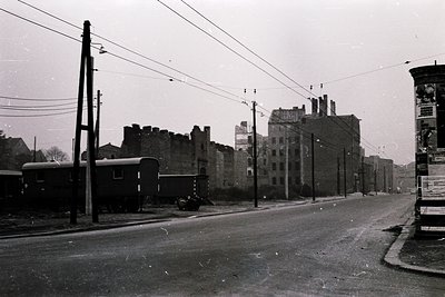 Mid-20th century urban street scene featuring a vintage railway carriage on tracks beside dilapidated brick buildings. Overhe...