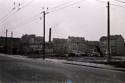 Black-and-white street scene showing post-war urban decay: multi-story brick buildings with bombed-out façades, exposed inter...
