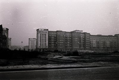 Mid-century Soviet-era apartment blocks with flat roofs and uniform balconies line a coastal road. Aged black-and-white photo...
