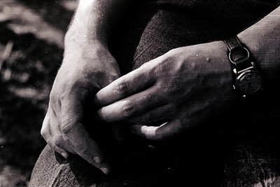 Close-up of hands clasped in a relaxed grip, wrist adorned with a vintage analog watch. Black-and-white composition suggests ...