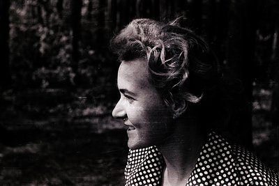 Black-and-white portrait of a woman with short, voluminous hair styled in a side part. She wears a polka-dot blouse with a hi...
