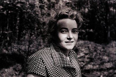 Black-and-white portrait of a woman in a polka-dot blouse, mid-20th century style. Her hair is styled in a voluminous, slight...