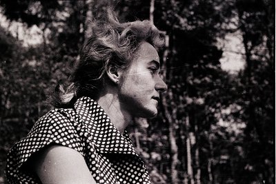 Portrait of a woman in a mid-century polka-dot blouse, set against dense forest foliage. Soft focus and monochrome suggest vi...