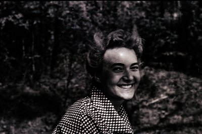 Vintage sepia-toned portrait of a woman with voluminous 1950s-style hairdo, wearing a polka-dot blouse. Outdoors setting with...
