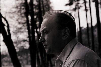 Portrait of a man in mid-profile, set against dense forest foliage. Lighting suggests late afternoon or early evening. Mid-ce...