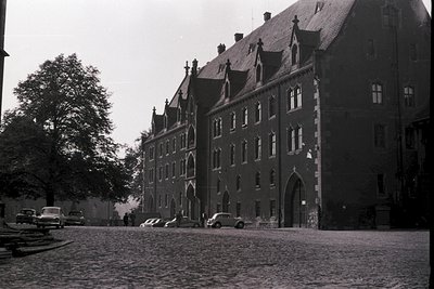 Historic Gothic-style building with steep gables and arched entryway, likely a university or institutional complex. Cobblesto...