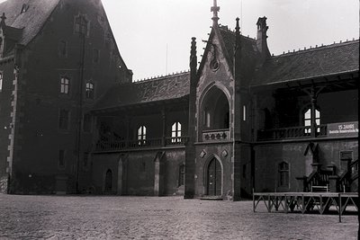 Black-and-white courtyard of a medieval-style building with Gothic arches, timber-framed upper floors, and a central stone ga...