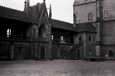 Gothic-style courtyard with stone arches, spiral staircases, and pointed windows—likely a historic European castle or monaste...