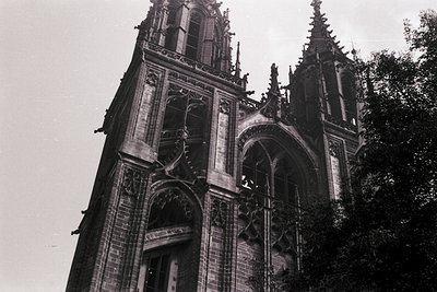 Gothic cathedral façade featuring pointed arches, intricate stone carvings, and twin spires. Dark brickwork contrasts with li...
