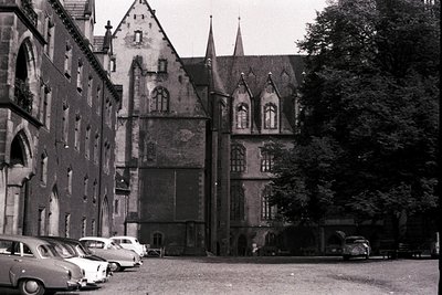 Historic European courtyard with Gothic Revival architecture—steepled roofs, arched windows, and weathered stone walls. Mid-2...