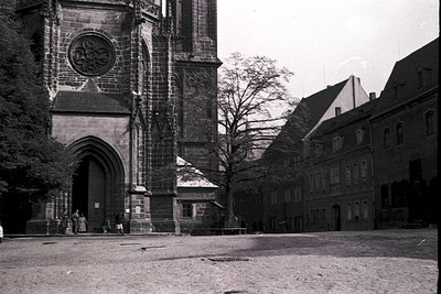 Black-and-white shot of a Gothic-style cathedral façade with pointed arches and ornate stonework, flanked by residential buil...