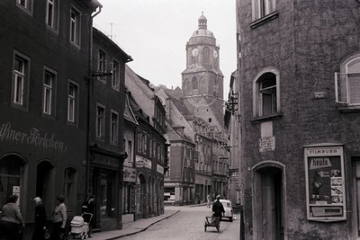 Historic European street scene with mid-20th century architecture. Prominent clock tower in background suggests central locat...