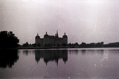 Vintage black-and-white shot of a grand Baroque-style castle reflected in a serene lake. Symmetrical towers and domes dominat...