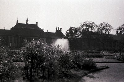 Neoclassical building with stepped gables and decorative spires in a formal garden, mid-20th century. Water feature in foregr...