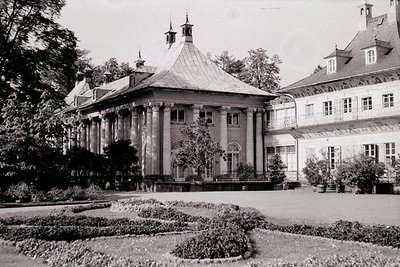 Neoclassical estate with symmetrical façade, central portico, and two peaked towers. Formal garden with geometric shrubbery a...
