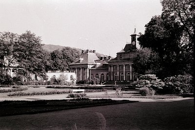 Neoclassical mansion with symmetrical façade, central entrance, and bell tower, set in meticulously landscaped gardens. Symme...