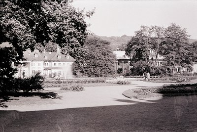 Symmetrical estate grounds featuring a central gravel path flanked by manicured hedges and mature trees. Prominent 2-story vi...