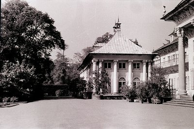 Neoclassical courtyard pavilion with domed roof, flanked by symmetrical columns and arched windows. Lush greenery and manicur...