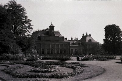 Neoclassical mansion with symmetrical façade, central clock tower, and gabled wings. Formal geometric gardens with manicured ...