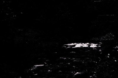 High-contrast black-and-white shot of a lone, partially obscured **moon** over a rugged, textured surface. Likely captured wi...