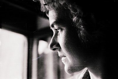 Black-and-white portrait of a person in profile, gazing upward with a contemplative expression. Soft lighting and slight grai...