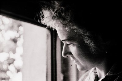 Portrait of an elderly woman in profile, captured in high-contrast black-and-white. She gazes intently at a blurred outdoor s...