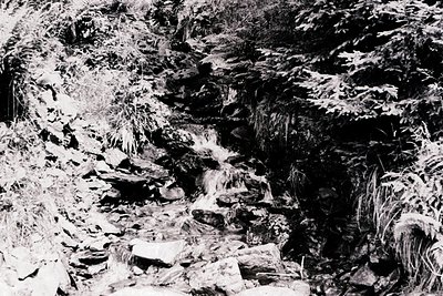 High-contrast black-and-white shot of a rugged, rocky riverbed with cascading waterfalls. The terrain features jagged limesto...
