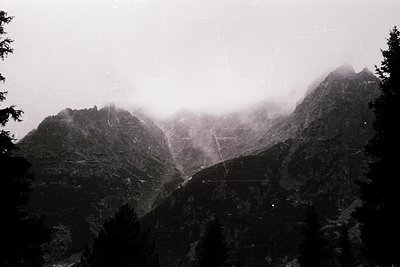 Misty alpine peaks shrouded in low-hanging clouds, with a lone cable or suspension line cutting diagonally across the scene. ...