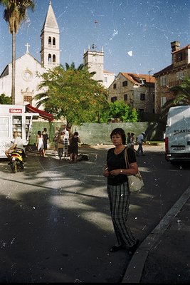 Vintage street scene featuring a woman in striped pants and a black top, standing near a "Tiraj" sign (likely a printing shop...