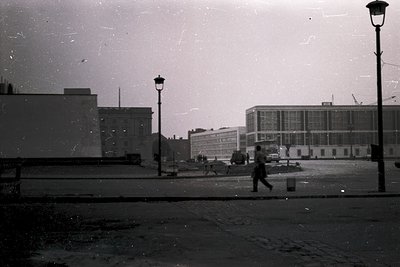 Vintage black-and-white street scene featuring Brutalist-style concrete buildings with grid-patterned windows, likely from th...