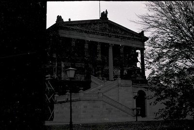 Neoclassical building with Corinthian columns and ornate entablature, captured in monochrome. Staircase leads to an elevated ...