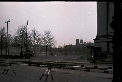 Vintage black-and-white street scene featuring early 20th-century urban design. Barren trees line a wide, empty boulevard fla...