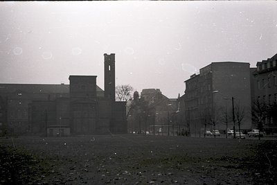 Black-and-white industrial site featuring a tall brick chimney and utilitarian brick buildings, likely from mid-20th century....