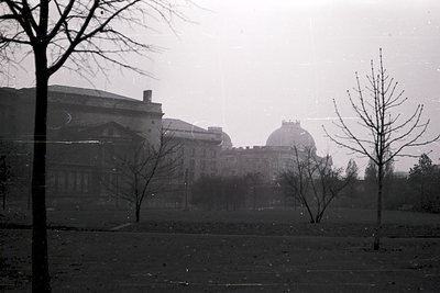 Vintage black-and-white shot of a grand neoclassical building complex partially obscured by mist, featuring columns and domed...