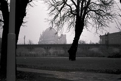 Black-and-white shot of a Soviet-era dome atop a high-rise building, partially obscured by bare winter trees and mist. Archit...