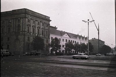 Neoclassical corner building with arched ground-floor entrance and decorative stonework, flanked by mid-20th century institut...