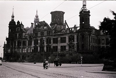 Damaged historic building with Gothic Revival architecture—noticeable spires, arched windows, and ornate stonework. Tram trac...