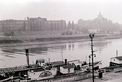 Black-and-white riverfront scene featuring a vintage steamboat labeled "Königstein" docked alongside a pier. Historic Europea...