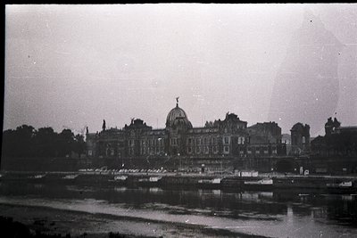 Grand neoclassical palace with domed roof, likely a government or royal building, reflected in shallow water. Surrounding tre...