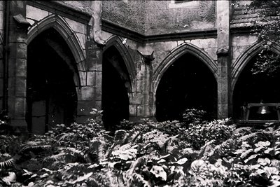 Gothic stone arches and vaulted ceilings of a ruined cloister, covered in snow and debris. Likely a medieval monastic complex...
