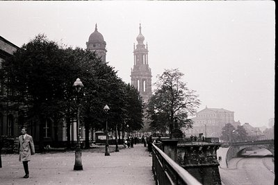 Vintage black-and-white street scene featuring twin domed towers of a grand cathedral flanked by classical buildings. Pedestr...