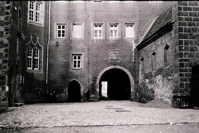 Historic stone courtyard entrance with Gothic Revival architecture—arched gateway flanked by brick walls and a central coat o...