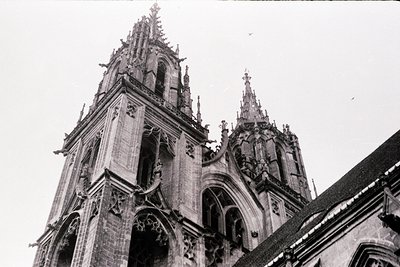 Gothic cathedral façade featuring twin spires with intricate stone tracery, rose window, and buttresses. Architectural detail...