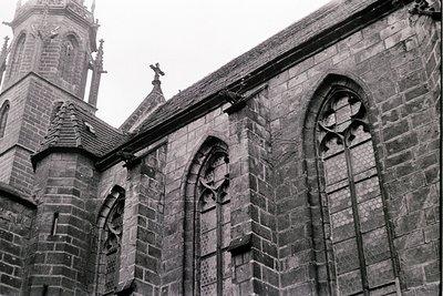 Gothic stone church façade featuring pointed arches, tracery windows, and a steeply pitched roof with decorative spires. Weat...