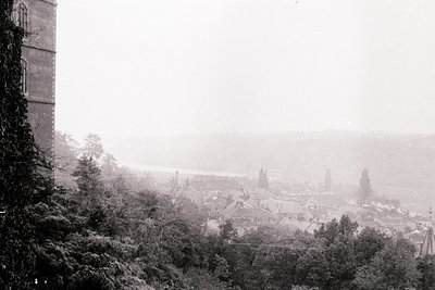 Black-and-white coastal town obscured by dense fog, with a prominent cylindrical tower on left. Low-angle perspective reveals...