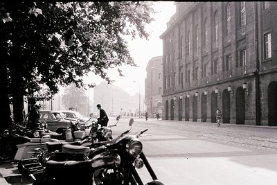 Classic black-and-white street scene featuring a grand, symmetrical building with arched windows and columns, likely institut...